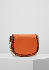 Malá oranžová crossbody taška s texturovaným povrchem, vybavená černým aksamitním lemováním a zlatým řetízkovým popruhem. Zaoblené víčko.