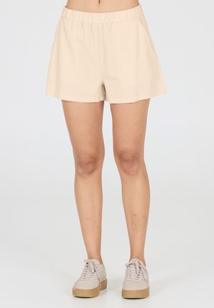 Beige katoenen shorts met een elastische tailleband, voorzien van een relaxte pasvorm en zonder zakken, gecombineerd met lichtgrijze sneakers op een effen achtergrond.