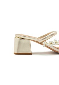 Sandalo con tacco spesso in oro metallico, dotato di cinturini incrociati e perle decorative lungo la soletta.