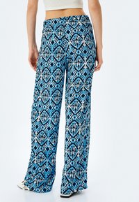 Blå mönstrade vida byxor med intrikata geometriska mönster i vitt och svart. Elastisk midja, lättviktig tyg och en slät textur.