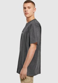 Grå kortærmet t-shirt lavet af blødt stof, med en afslappet pasform og minimalisk logo detail på forsiden, sat mod en neutral baggrund.