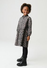 Haljina s leopard uzorkom s kopčanjem na gumbe, dugim rukavima i strukom nabranim u naborima. Uparena s crnim leginzima i robusnim čizmama.