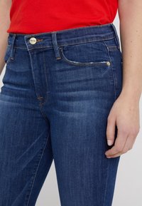 Jeans de mezclilla azul oscuro con corte slim, con cierre de botón de metal, un ligero desgaste y diseño clásico de cinco bolsillos.