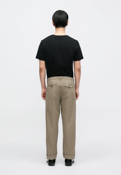 Μαύρο βαμβακερό t-shirt με κοντά μανίκια και λαιμόκοψη, συνδυασμένο με μπεζ παντελόνι φαρδιάς γραμμής που διαθέτει δύο τσέπες στην πλάτη και γυρισμένα μανίκια.