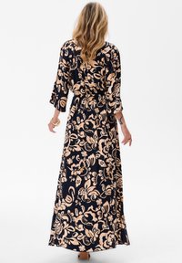 Kwiatowa sukienka maxi z granatowym tłem i jasnobeżowymi wzorami roślinnymi, z długimi rękawami, marszczoną w talii i swobodnym dołem.