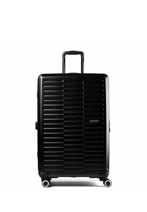 Schwarzer Hartschalenkoffer mit horizontalen Rillen, ausgezogenem Teleskopgriff, vier Drehrollen und American Tourister-Logo vorne.