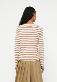 Dlhý rukáv pruhovaného topu s striedavými hnedými a bielymi vodorovnými pruhmi. Bavlnená látka, okrúhly výstrih a logo na chrbte.