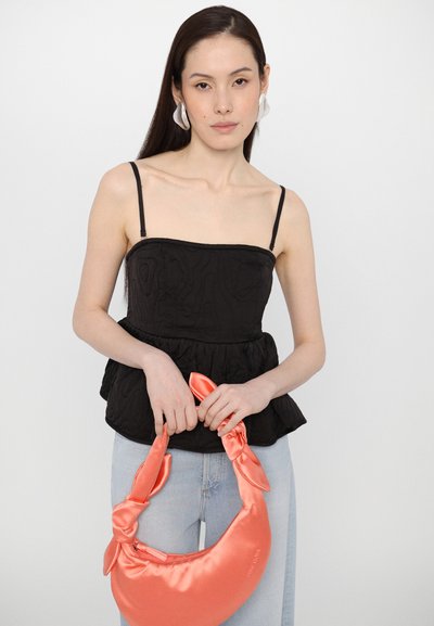 Black quilted crop top with thin straps and a peplum hem, paired with a glossy coral satin handbag featuring knot accents. Light denim jeans.