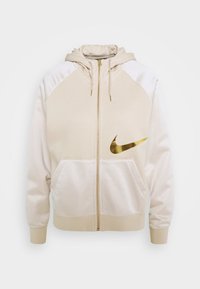 Beige hoodie med en gul Nike-logotyp. Har en hel dragkedja, raglanärmar, två framfickor och en mjuk textur.