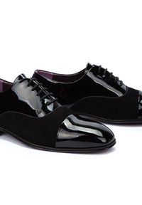 Zapatos negros con punta de charol brillante y cuerpo de ante, con cordones negros y un forro interior púrpura.