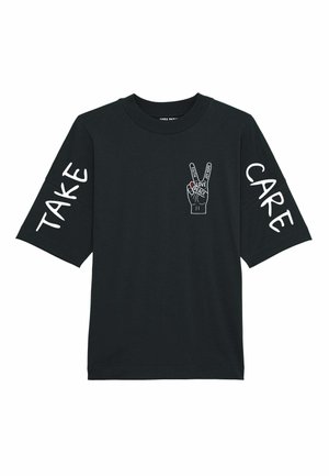 T-shirt noir à manches courtes avec du texte blanc indiquant "TAKE" et "CARE" sur les manches, avec un graphique de signe de paix à l'avant.