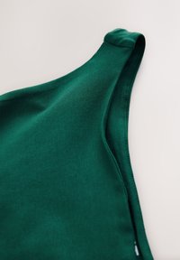 Gros plan d'une bretelle de débardeur en tissu vert avec une couture nette sur fond blanc.