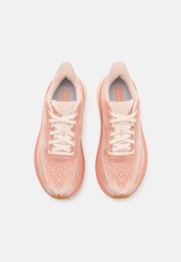 Zapatillas deportivas de color rosa claro con una parte superior texturizada y transpirable. Presentan un diseño con patrón, cordones blancos y una suela acolchada.