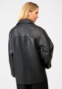 Sort læderjakke med krave. Designet har en afslappet pasform og en glat tekstur, der fremviser minimale syninger.