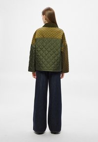 Πράσινο και ελιάς μπουφάν με ραφές σε σχέδιο ρόμβου, γιακά και φαρδιά εφαρμογή, συνδυασμένο με τζιν παντελόνι με φαρδιά πόδια.