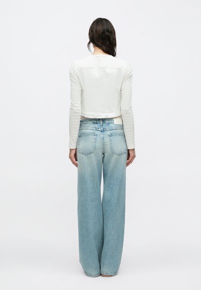 Λευκό μακρυμάνικο cropped τοπ με στρογγυλή λαιμόκοψη, συνδυασμένο με ψηλόμεσα, ανοιχτό μπλε, φαρδιά τζιν παντελόνια με ελαφριά ξεθώριασμα και πίσω τσέπες.