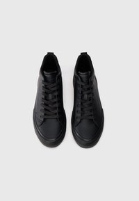 Μαύρα αθλητικά παπούτσια με λείο δερμάτινο επάνω μέρος, επίπεδα κορδόνια, στρογγυλή μύτη και υφή στη σόλα. Διαθέτουν ελάχιστη επωνυμία στη γλώσσα του παπουτσιού.