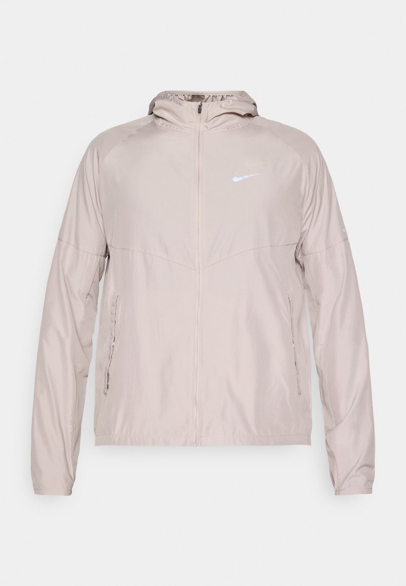 Leichtbeige Nike-Jacke aus leichtem Material, mit einem Frontreißverschluss, Kapuze und seitlichen Taschen. Reflektierendes Logo auf der Brust.