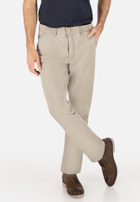 Beige cotton chinos with a straight cut, featuring a button closure, side pockets, and worn with brown lace-up shoes.