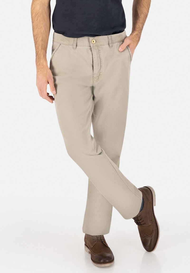 Beige cotton chinos with a straight cut, featuring a button closure, side pockets, and worn with brown lace-up shoes.
