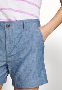 Leren denim shorts in lichtblauwe stof met een zachte textuur. Voorzien van een knoopsluiting en zijzakken, ontworpen voor comfort en casual draaggemak.