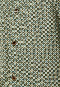 Korte mouwen shirt in lichtblauw, crème, en bruin geometrisch patroon, met bruine knopen en een textuurstof.