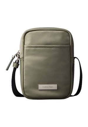 Kompaktna maslinasto zelena torbica na preklop s prednjim džepom, crnim podesivim remenom, zatvaračem na patentni zatvarač i pločicom s logotipom Calvin Klein.
