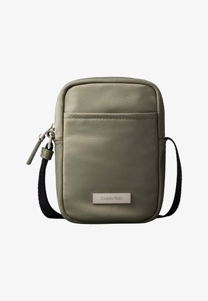 Sac bandoulière compact vert olive avec poche avant, sangle noire réglable, fermeture zippée et plaque logo Calvin Klein.