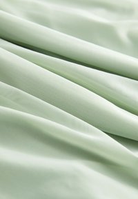 Tissu vert clair doux avec une texture fine, montré en gros plan avec des plis et un drapé délicat.