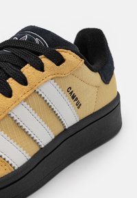 Sárga és fekete sneaker, textúrált felsőrésszel, három fehér csíkkal, gumi talppal és "CAMPUS" felirattal az oldalon.