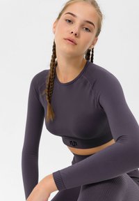 Long-sleeve purple sports top with ribbed hem, seamless design, and textured accents. Made from stretchy, breathable fabric for comfort.