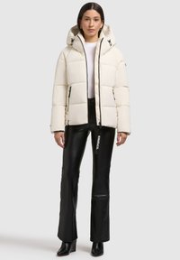 Off-white Daunenjacke mit Kapuze, featuring ein gestepptes Design und kontrastierenden schwarzen Reißverschlüssen. Kombiniert mit eng anliegenden schwarzen Lederhosen.