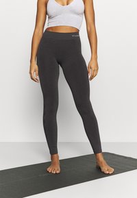 Leggings gris ajustés avec une texture lisse et une taille haute, présentant un logo discret sur la taille et sans motifs ou accents visibles.