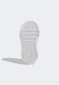 Bílá podrážka tenisky s texturovaným vzorem protiskluzu se kruhovými a vodorovnými liniemi a malým logem na boku.