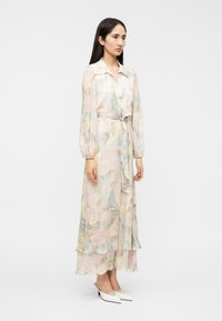 Ρομαντικό, μακρύ φόρεμα με απαλό παστέλ λουλουδένιο σχέδιο, μπαλόν μανίκια και ζώνη στη μέση. Διαθέτει στρωμένο τελείωμα και ελαφρύ, ημιδιάφανο ύφασμα.