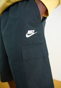 Pantaloni cargo neri realizzati in un tessuto strutturato, dotati di una tasca laterale e di un logo Nike bianco sulla coscia.