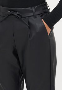 Zwarte nep leren broeken met een cinched tailleband, voorplooien en zijzakken. Beschikt over een trekkoord detail.