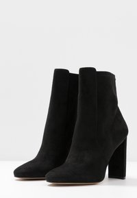 Bottines en daim noir avec un bout pointu et un talon bloc haut. Design sans coutures avec une texture lisse et sans éléments métalliques visibles.