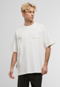 Hvit oversized bomull t-skjorte med korte ermer, med lysegrønne tekstdetaljer på brystet og en avslappet passform.