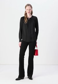 Blusa nera a maniche lunghe con bottoni davanti e scollatura rotonda. Abbinata a pantaloni neri aderenti e una piccola borsa rossa.