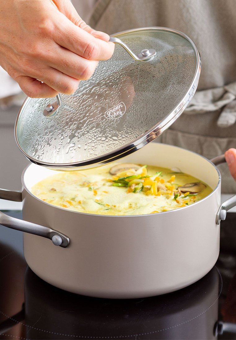 Hellbeige Kochtopf mit einem Glasdeckel, silbernen Griffen und Kondenswasser auf dem Deckel. Enthält eine Mischung aus Suppe und Gemüse.