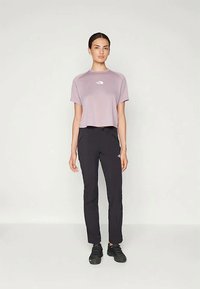 Világoslila crop top, kis fehér logóval, fekete, tapered fazonú nadrággal, oldalsó zsebekkel, fekete sportcipővel párosítva.