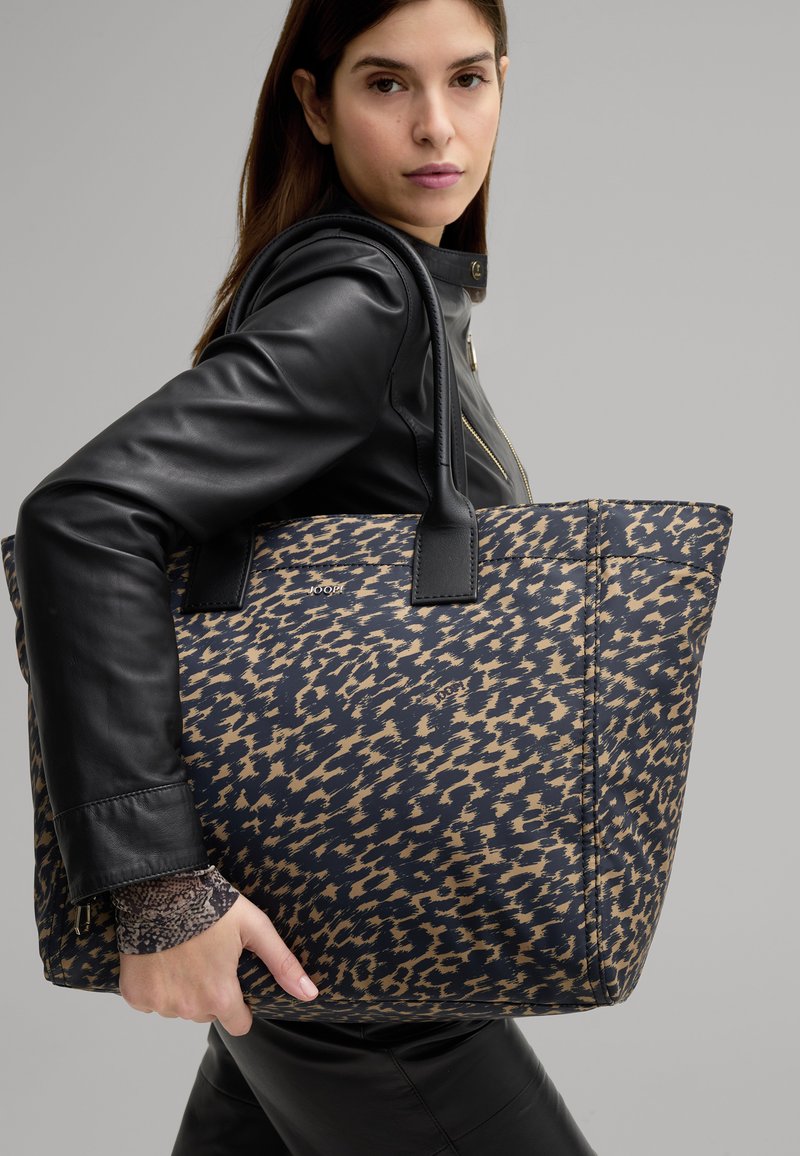 Large tote bag featuring a navy and beige leopard print design, made of durable fabric, with black leather handles and subtle branding.