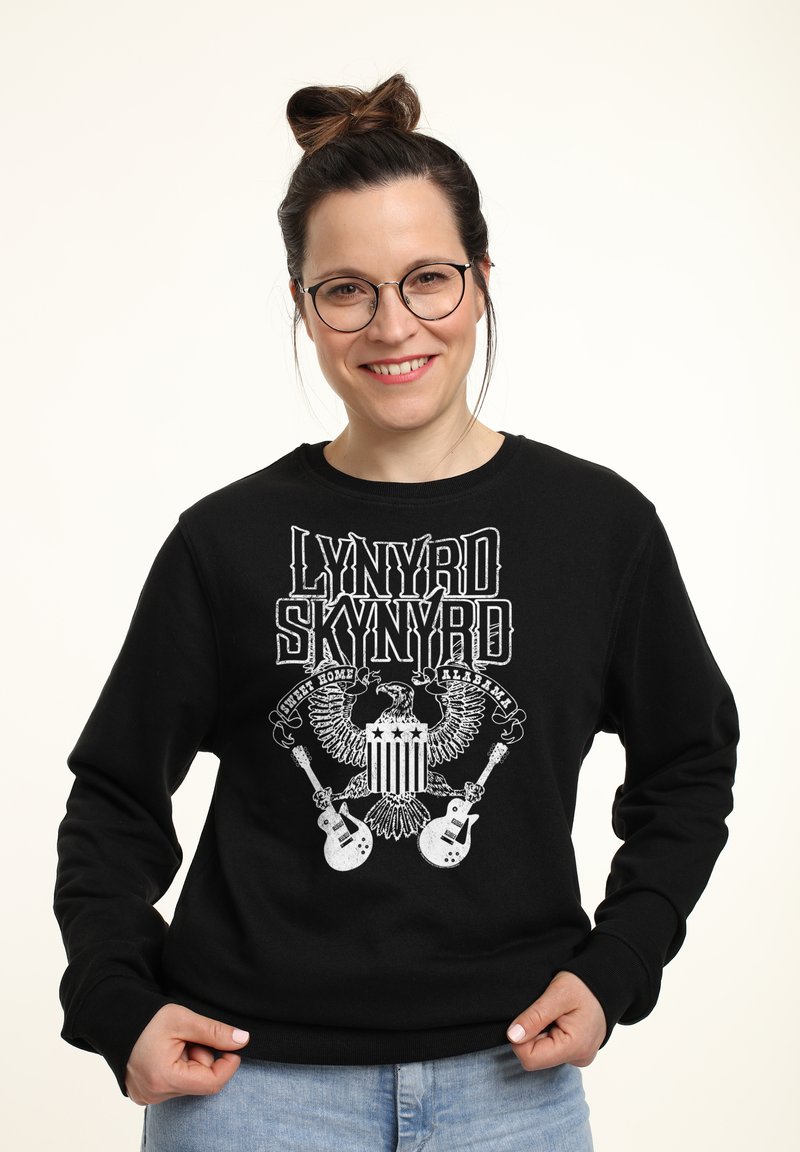 Sudadera negra con un estampado gráfico de un águila, guitarras y el texto "LYNYRD SKYNYRD". Puños acanalados y cuello redondo. Textura suave.