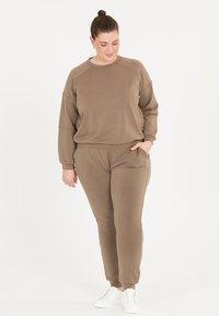 Brun sweatshirt och matchande joggare, gjorda av mjukt tyg. Sweatshirten har en rund halsringning och raglanärmar; joggarna har sidofickor och mudd.