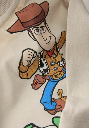 Beige T-Shirt mit einem Cartoon-Cowboy, der einen braunen Hut, ein kariertes Hemd und blaue Hosen trägt. Das Design enthält Sheriffsabzeichen und leichte Akzentuierungen.
