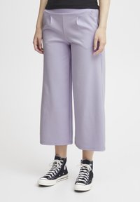 Lila wijde broek van zacht materiaal, met een platte tailleband, twee voorkezen en een omgeslagen zoom. Gepaard met zwarte hoge sneakers.
