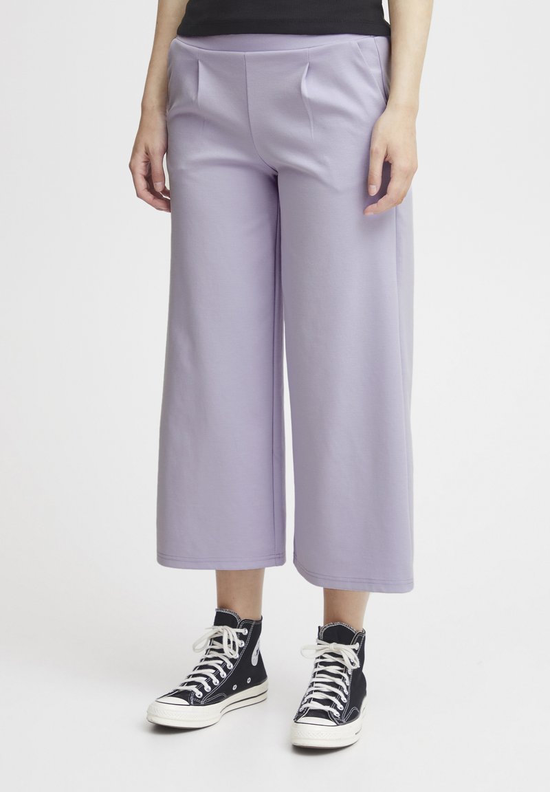 Lila wijde broek van zacht materiaal, met een platte tailleband, twee voorkezen en een omgeslagen zoom. Gepaard met zwarte hoge sneakers.