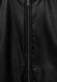 Gros plan d'un vêtement en cuir noir avec une fermeture éclair métallique argentée centrée et une surface en cuir texturée visible.