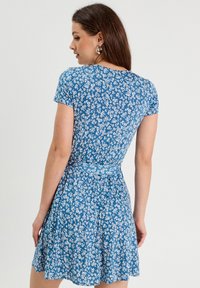 Vestido floral azul con mangas cortas, una cintura ajustada y una falda acampanada. Flores blancas crean un patrón contrastante en toda la tela.